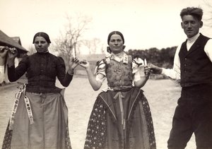 Deux dames et un homme, en costumes traditionnels hongrois, se tenant par la main dans une danse, tenant des bougies